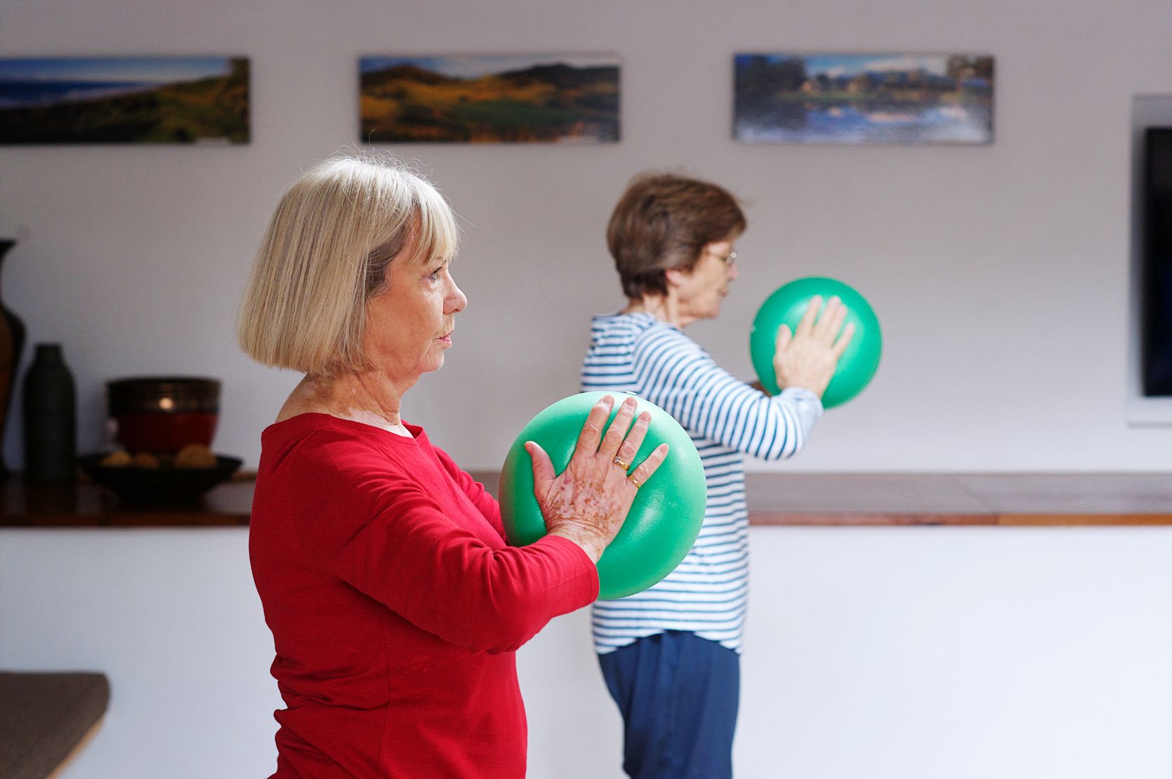 Zwei Frauen machen Pilates im Stehen mit einem kleinen Ball