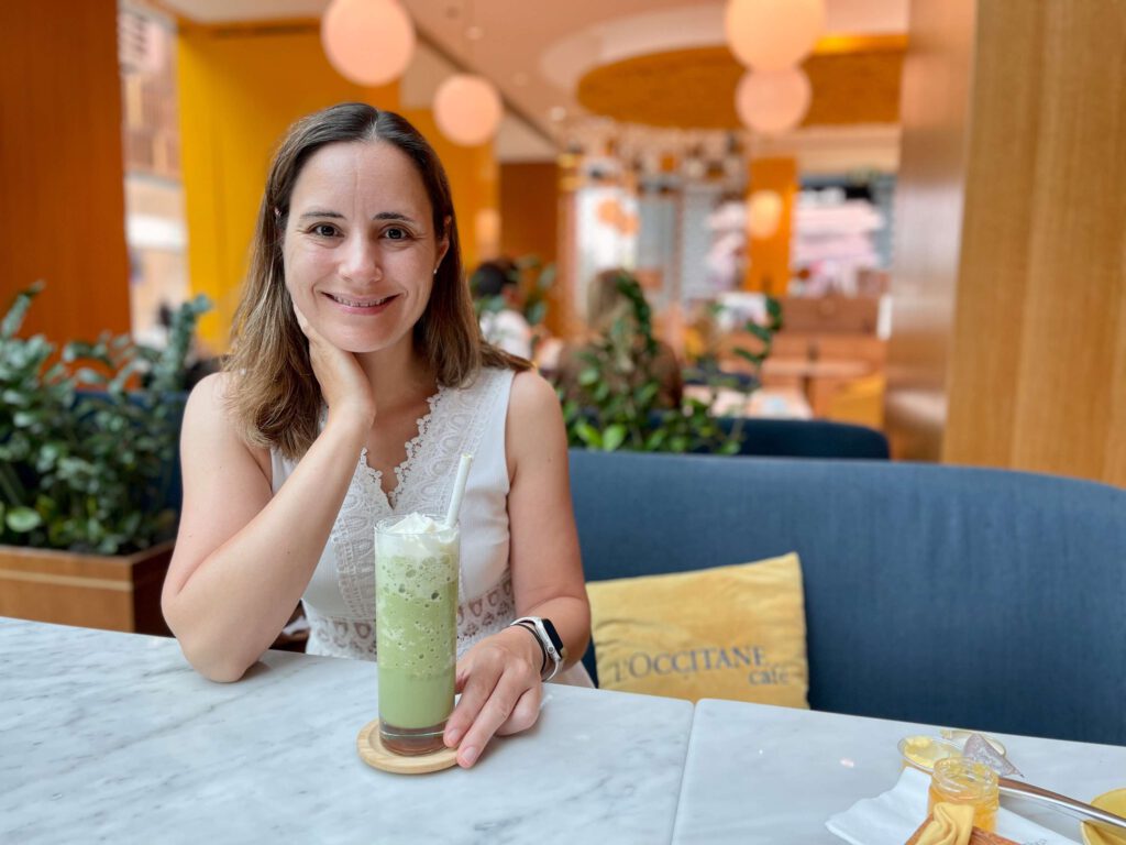 Frau Sitzt In Einem Café Mit Einem Getraenk Und Laechelt In Die Kamera.