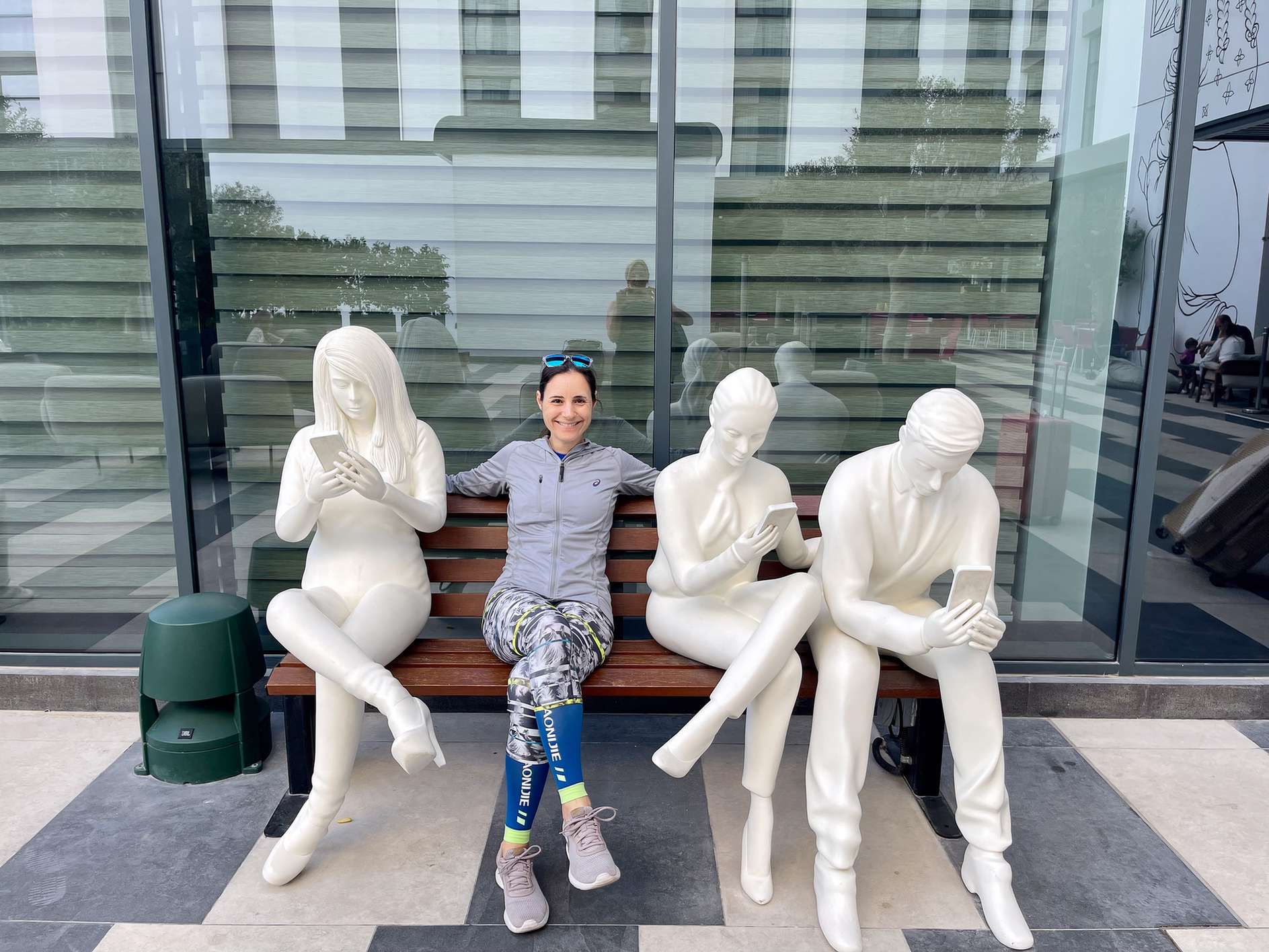 Woman sitting on a bench between white figures in front of a modern building.