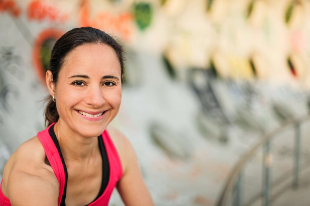 Laechelnde Frau In Sportkleidung Vor Bunter Wand.