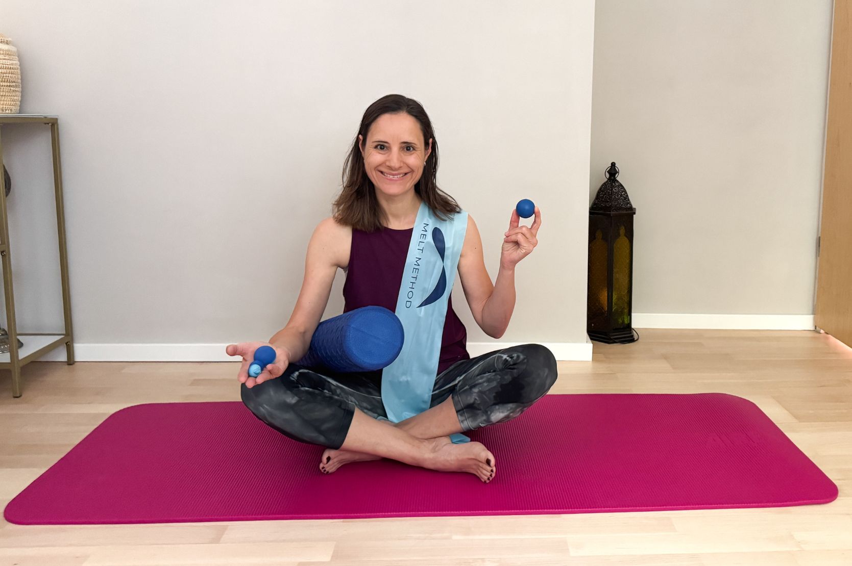 Woman is sitting on a fascia roller holding a small ball in her hand