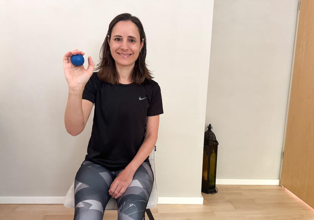 Frau sitzt auf Stuhl und drückt einen kleinen blauen MELT Ball mit der Hand
