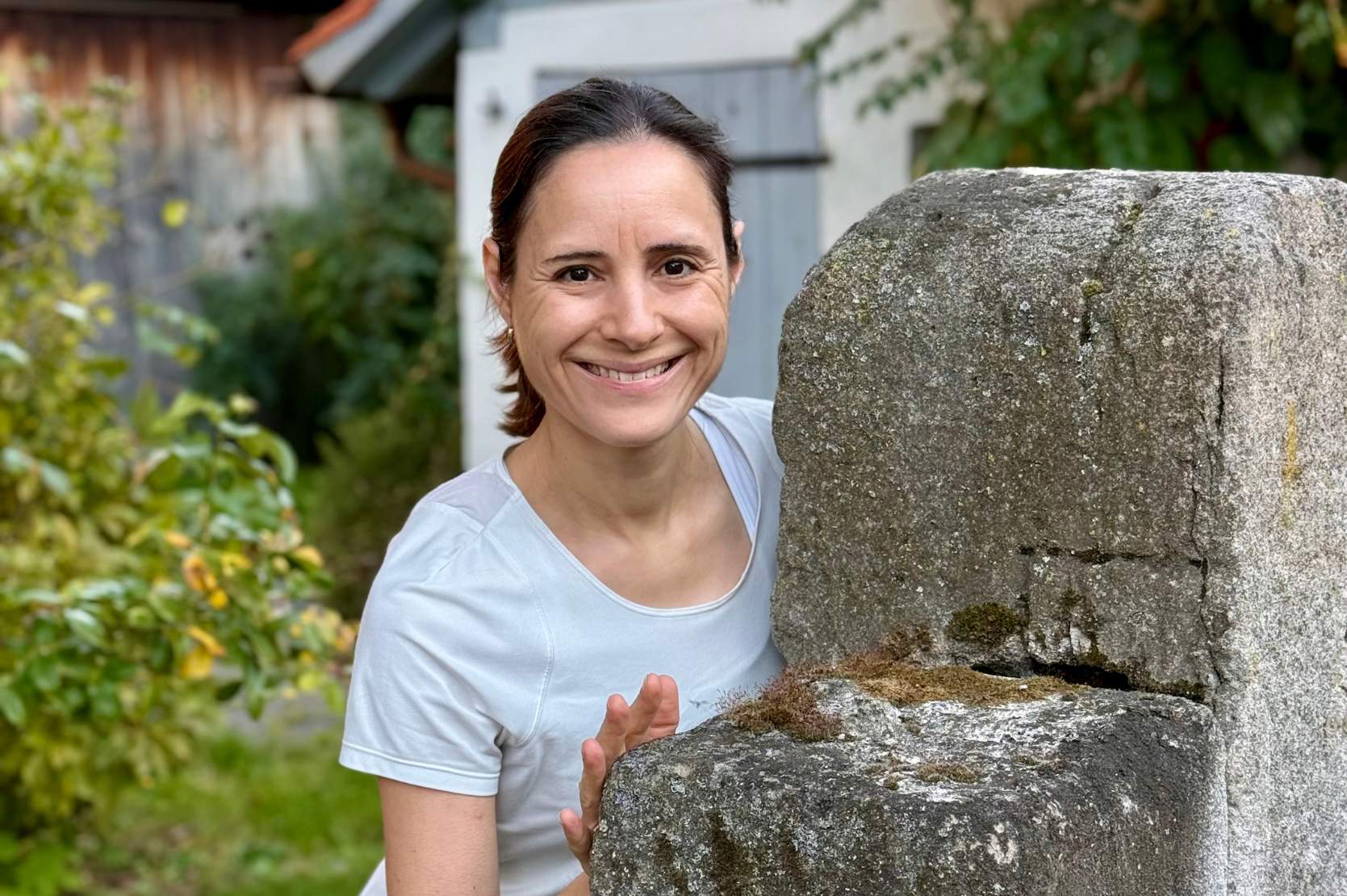 Frau steht hinter einem großen Stein und lächelt in die Kamera