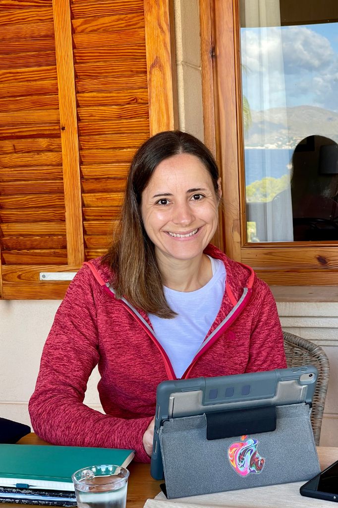 Lächelnde Frau sitzt vor Tablet und schaut in die Kamera